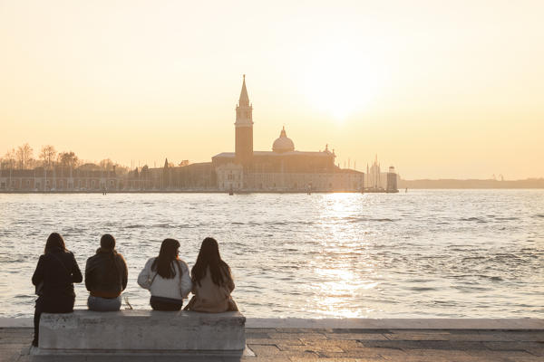 a group of  tourists admire the sunset towards the island of San Giorgio maggiore from the banks of the Grand Canal, Venice, Veneto, Italy