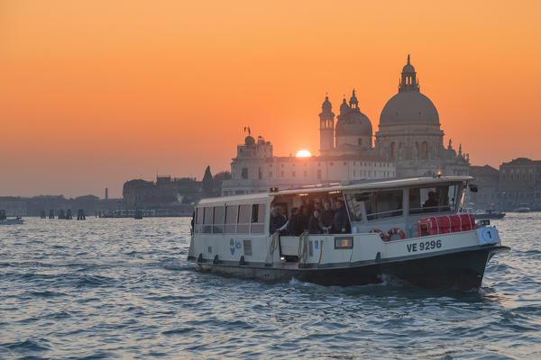 Venetian Vaporetto on the Grand Canal at sunset with Basilica of Saint Mary of Health, in background, Punta della Dogana, Venice, Veneto, Italy
