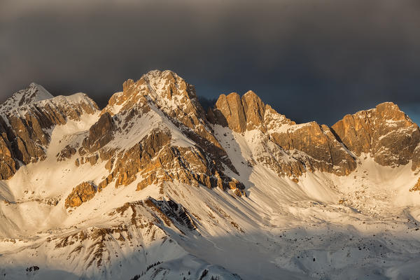 A fiery winter sunset towards the Sasso di Valfredda. From the left Punta Jigole, Sasso Vernale, Cima Ombrettola, Sasso Valfredda and Formenton. Behind them, covered by clouds the immense south face of the Marmolada. Dolomites, Italy