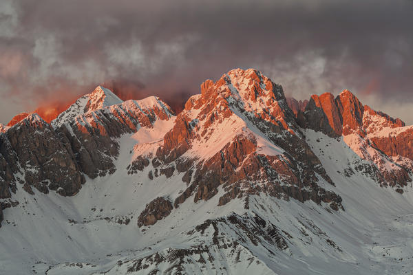 Europe, Italy, Veneto, Dolomites. Fiery winter sunset towards the Sasso di Valfredda as seen from Col Margherita.
From the left Punta Jigole, Sasso Vernale, Cima Ombrettola, Sasso Valfredda and Formenton, in the background covered by clouds the immense south face of the Marmolada.