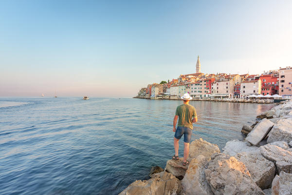 Rovinj - Rovigno, tourist on the rocks of the pier admires the splendid old town, Istria, Adriatic coast, Croatia (MR)