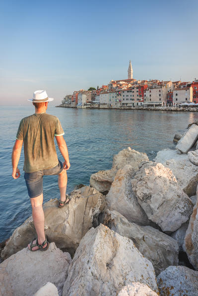 Rovinj - Rovigno, tourist on the rocks of the pier admires the splendid old town, Istria, Adriatic coast, Croatia