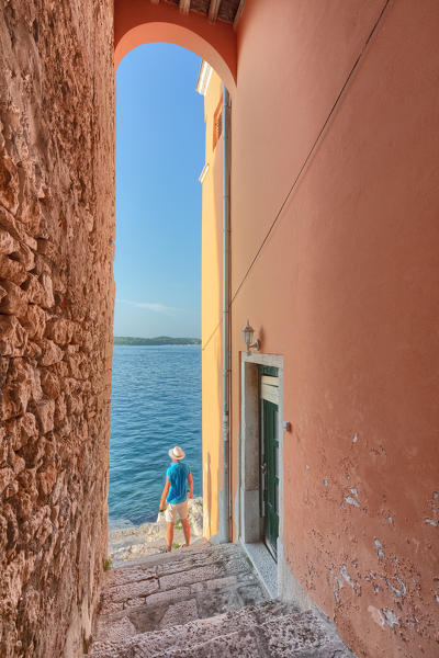 small arched opening overlooking the sea along the streets of Rovinj, tourist admires the view, Rovinj, Istria, Croatia (MR)