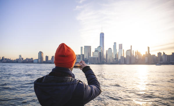 A man admiring Manhattan skyline at sunrise from New Jersey coastline. New York, USA.