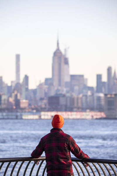 A man admiring Manhattan skyline at sunrise from New Jersey coastline. New York, USA.