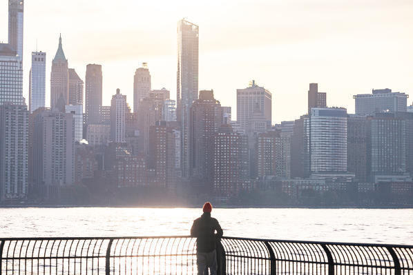 A man admiring Manhattan skyline at sunrise from New Jersey coastline. New York, USA.