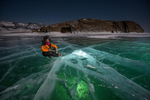 foto  - A person sitting over the transparent ice at the night at lake Baikal, Irkutsk region, Siberia, Russia