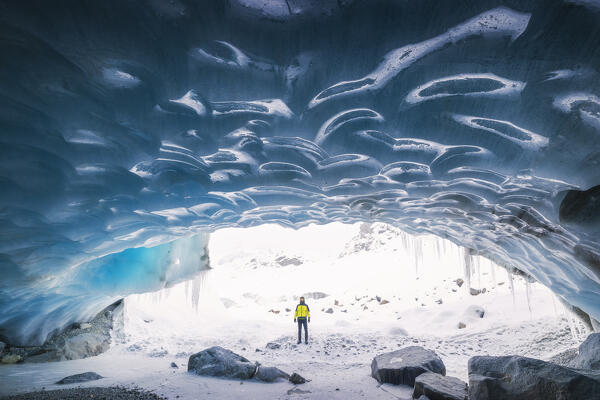 foto  - A trekker observes the entrance of an ice cave at Morteratsch glacier during winter, Bernina Valley, Grigioni, Switzerland, Western Europe