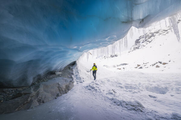 foto  - A trekker observes the entrance of an ice cave at Morteratsch glacier during winter, Bernina Valley, Grigioni, Switzerland, Western Europe